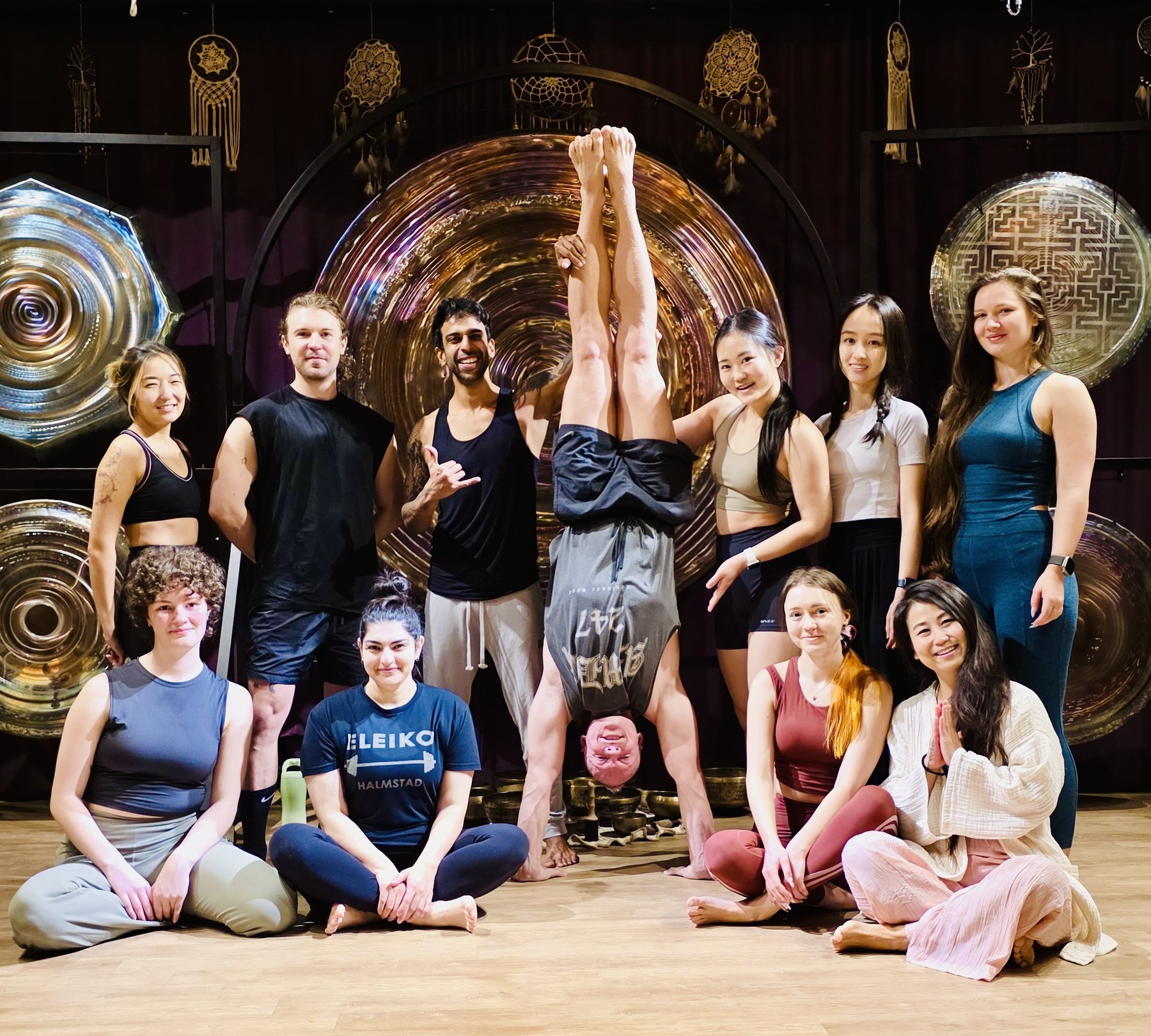 A handstand workshop group gathered in front of large gongs after practice